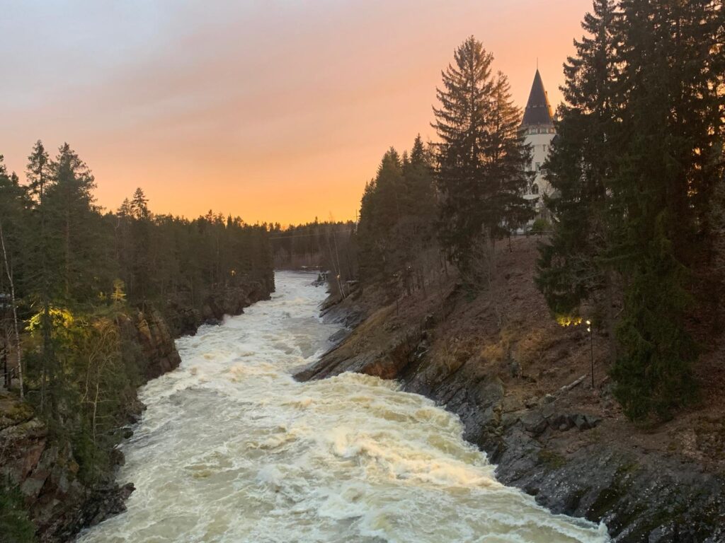Kuohuva Imatrankoski sekä Imatran valtionhotelli laskevan auringon valossa.